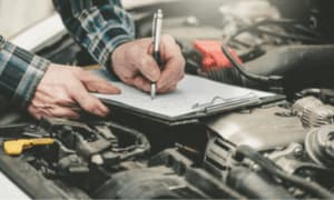 mani di un meccanico scrivono su un blocco poggiato sul motore di un'auto